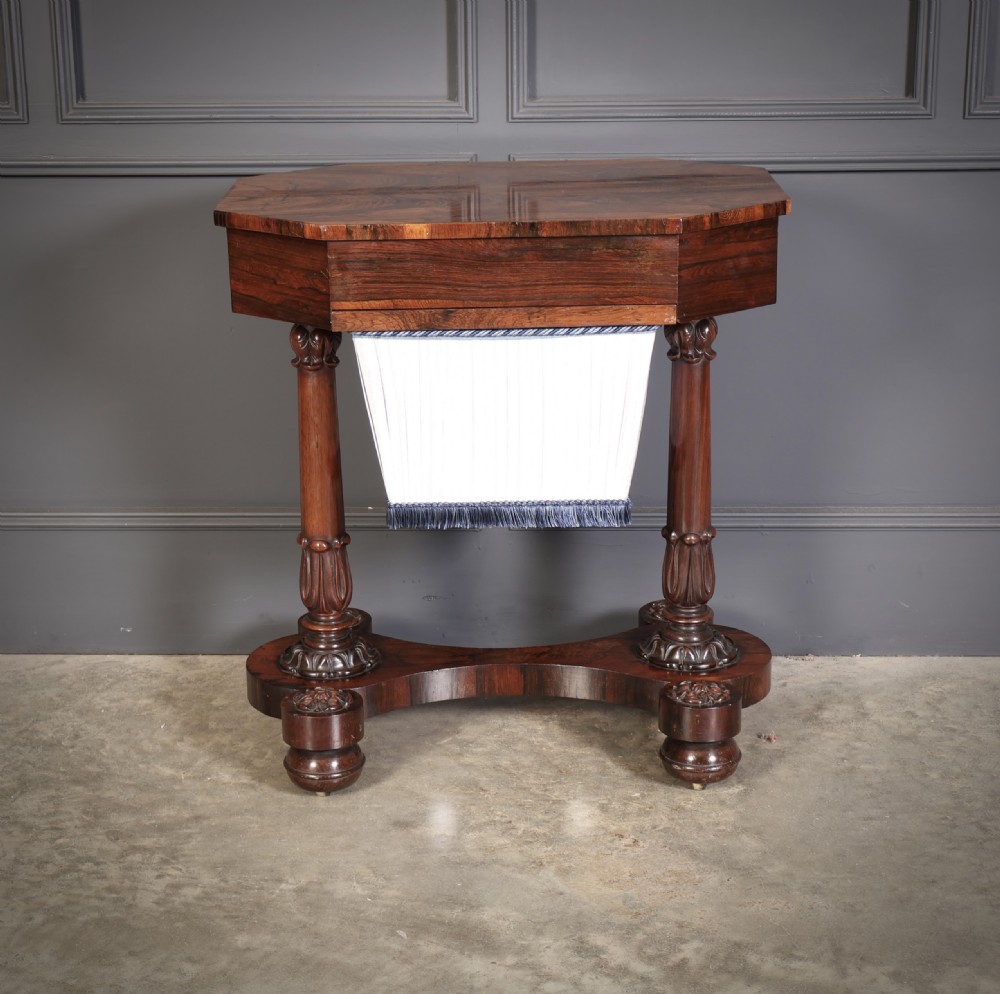 A William IV rosewood sewing table featuring an octagonal hinged top, a pleated fabric work basket, and carved twin column supports on a plinth base. View XII