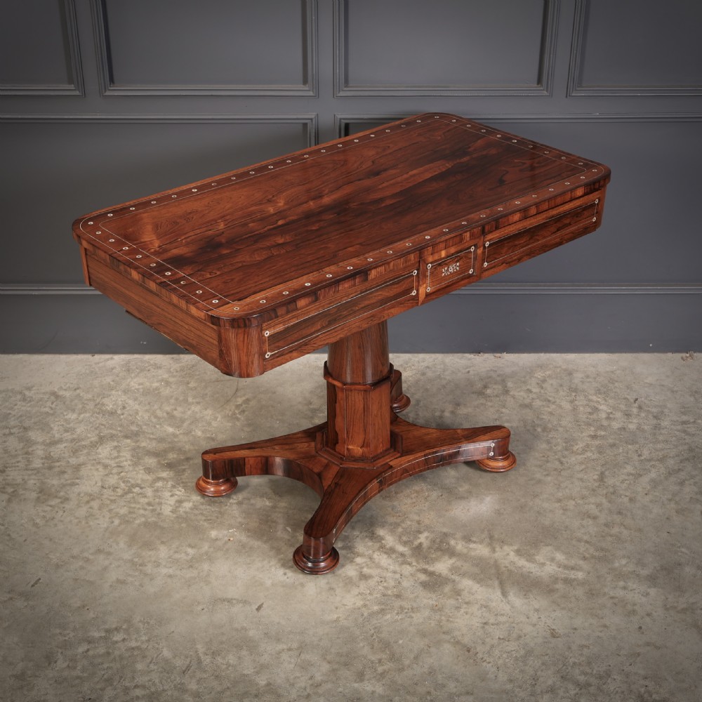 A Regency rosewood library table featuring brass stringing, dot inlays, frieze drawers, and a central pedestal support on a four-star base.