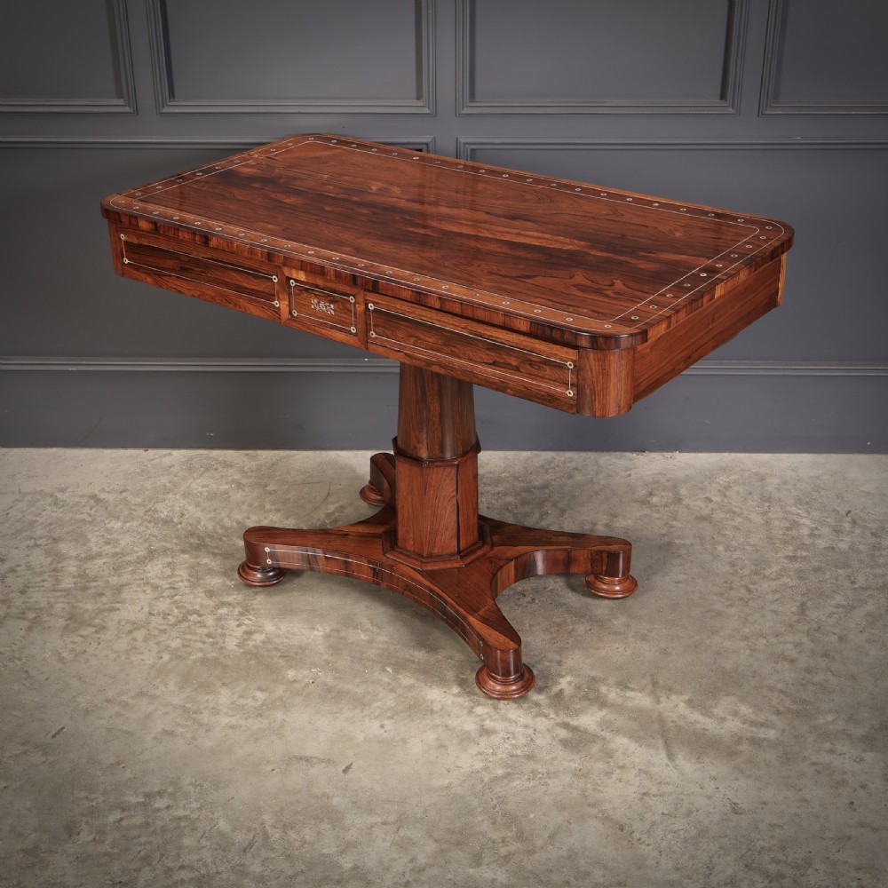 A Regency rosewood library table featuring brass stringing, dot inlays, frieze drawers, and a central pedestal support on a four-star base. View IX