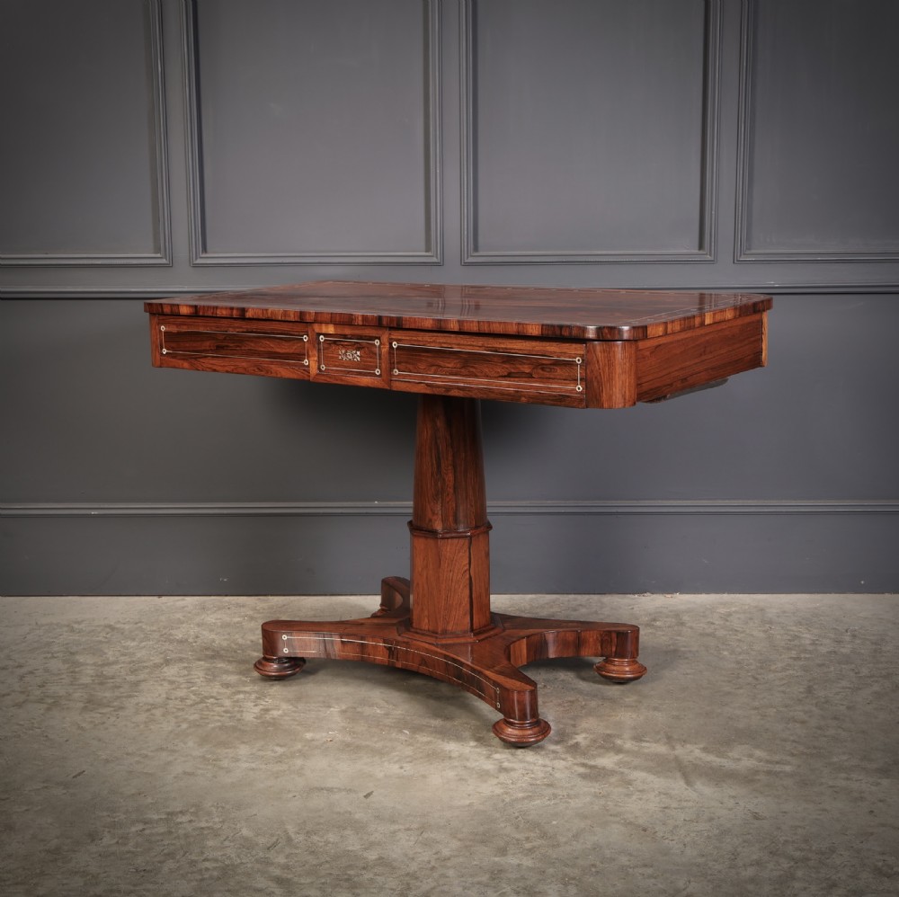 A Regency rosewood library table featuring brass stringing, dot inlays, frieze drawers, and a central pedestal support on a four-star base. View X