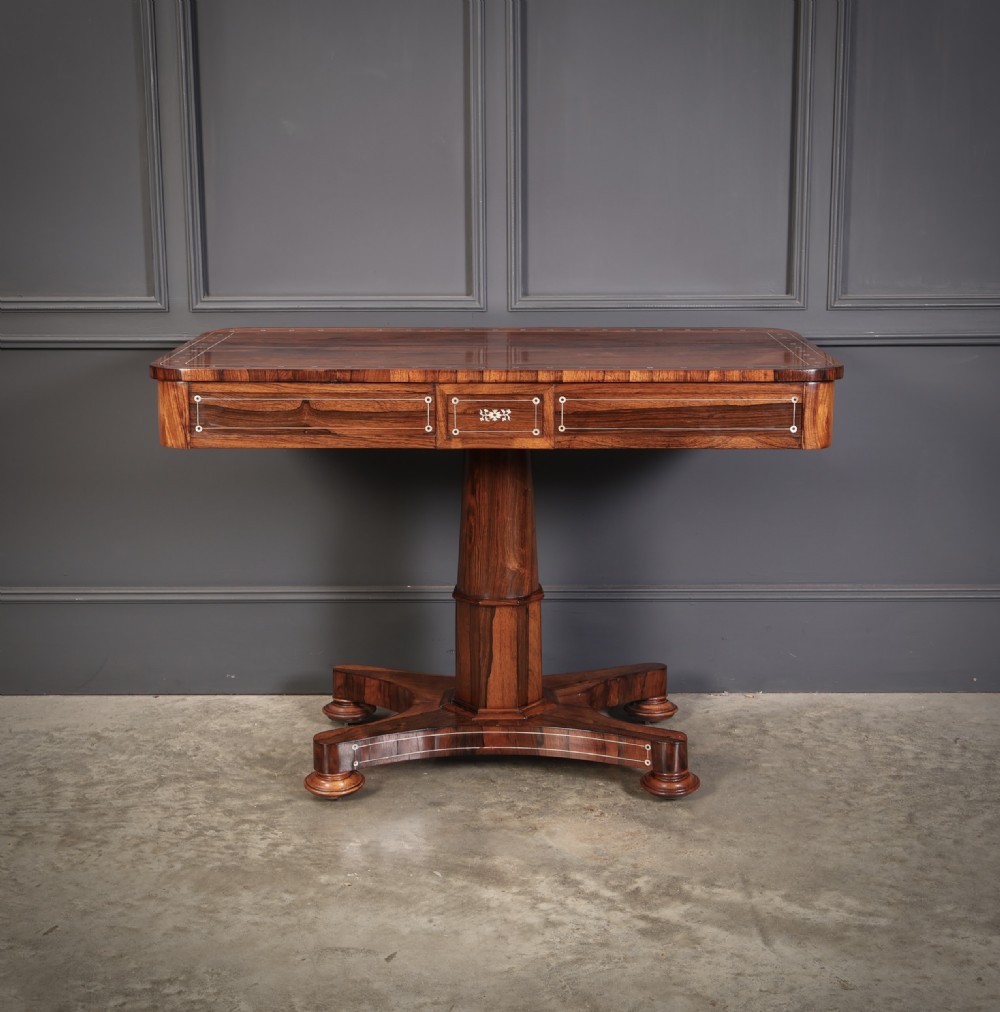 A Regency rosewood library table featuring brass stringing, dot inlays, frieze drawers, and a central pedestal support on a four-star base. View XVI