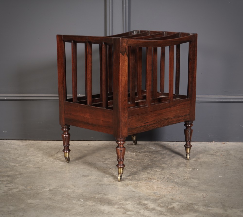 A William IV rosewood canterbury featuring four vertical slatted compartments, a single base drawer, turned legs, and brass castors.