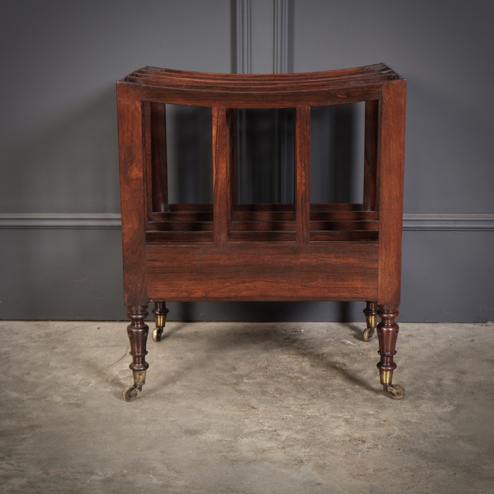 A William IV rosewood canterbury featuring four vertical slatted compartments, a single base drawer, turned legs, and brass castors. View X