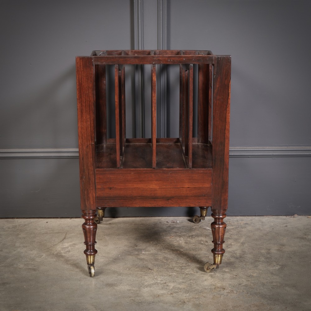 A William IV rosewood canterbury featuring four vertical slatted compartments, a single base drawer, turned legs, and brass castors. View XI