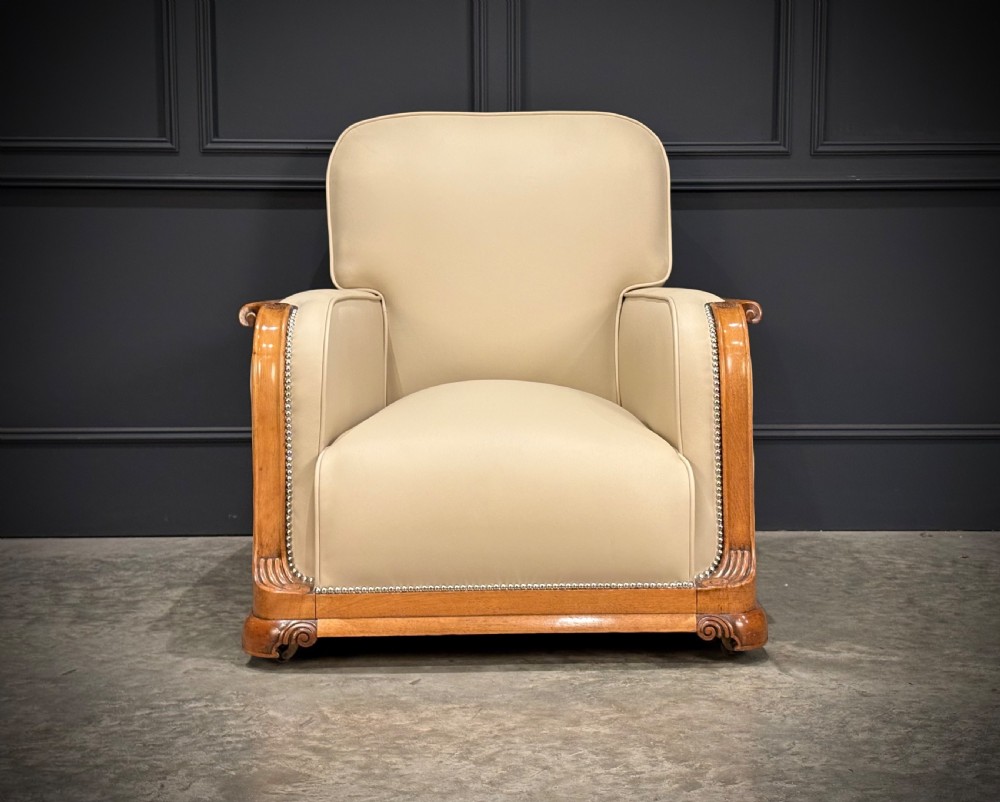 A pair of Art Deco armchairs featuring cream leather upholstery, polished walnut arm supports with scroll details, and metal studwork trim. View IV