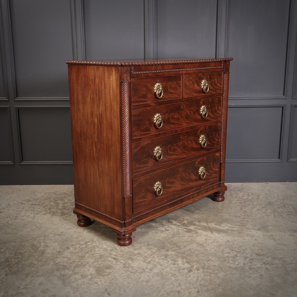 A nineteenth-century Scottish flame mahogany chest of drawers featuring twist-turned side columns, five graduated drawers with brass ring handles, and turned feet.