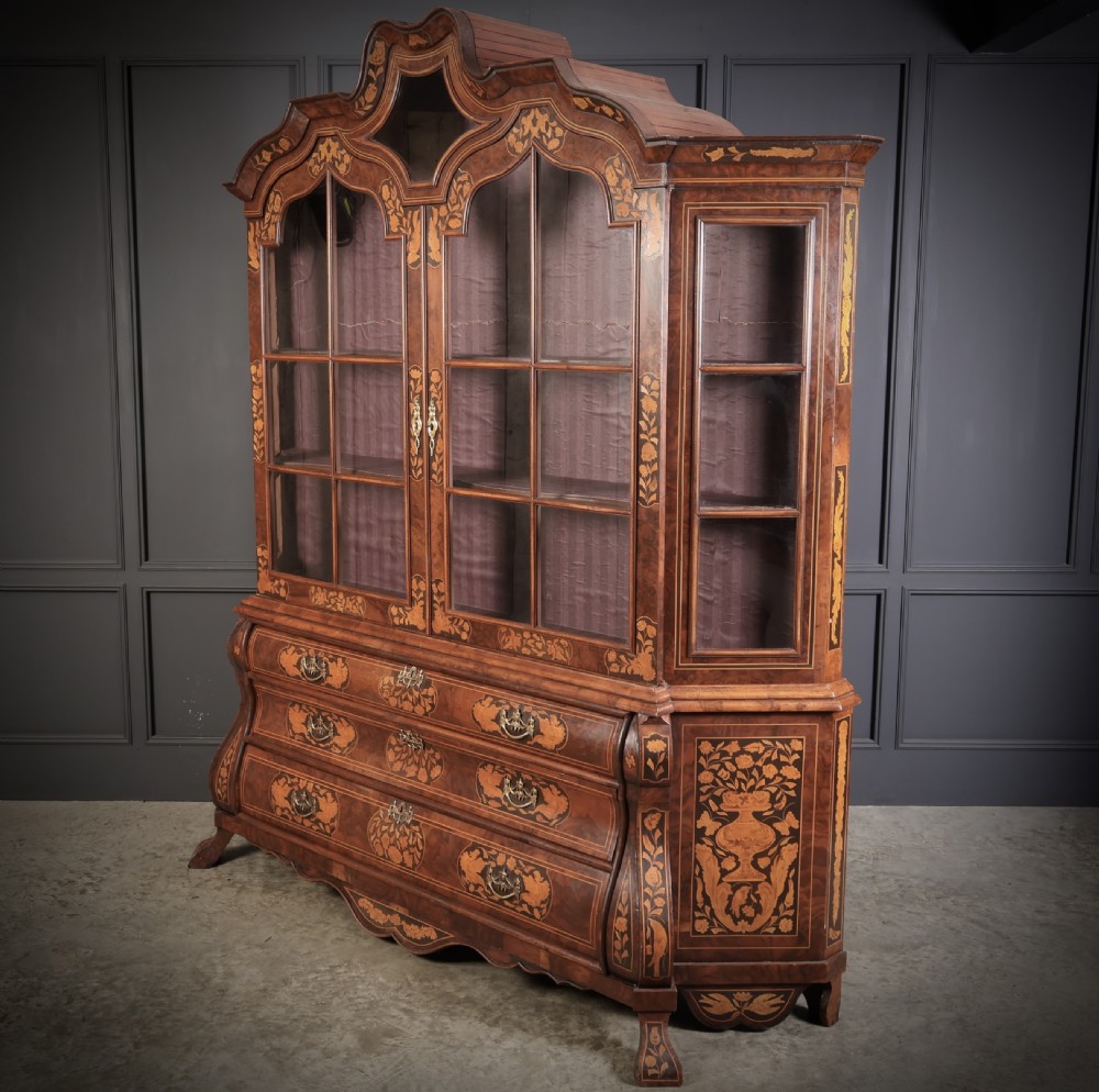A Dutch Baroque style walnut display cabinet featuring floral marquetry, a glazed double-door upper section, and a three-drawer bombe base. View V