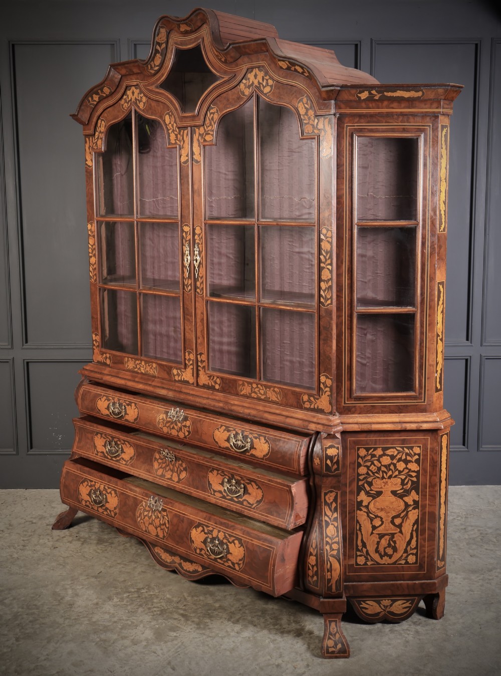 A Dutch Baroque style walnut display cabinet featuring floral marquetry, a glazed double-door upper section, and a three-drawer bombe base. View III