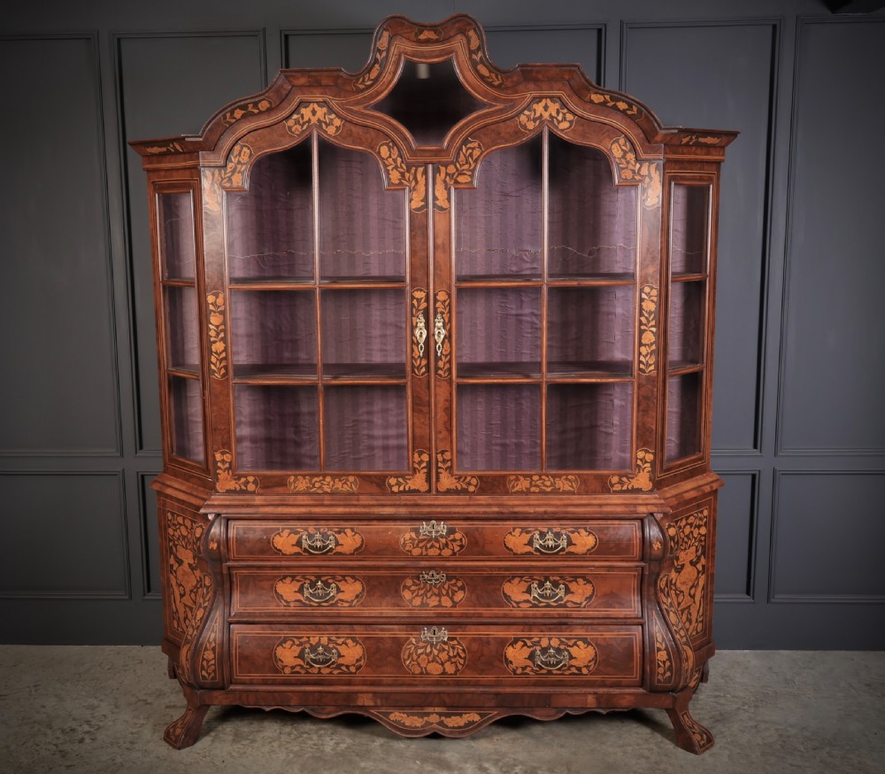 A Dutch Baroque style walnut display cabinet featuring floral marquetry, a glazed double-door upper section, and a three-drawer bombe base. View II