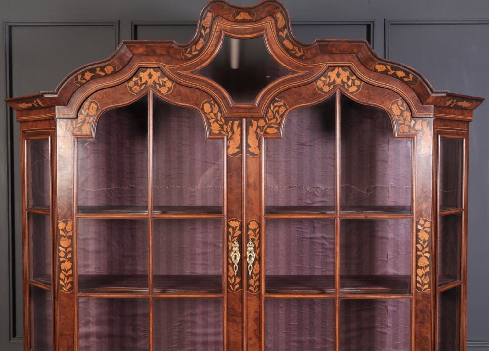 A Dutch Baroque style walnut display cabinet featuring floral marquetry, a glazed double-door upper section, and a three-drawer bombe base. View VIII