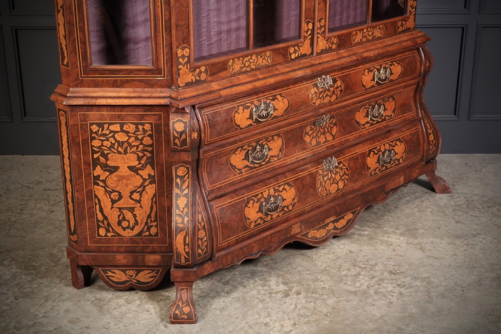 A Dutch Baroque style walnut display cabinet featuring floral marquetry, a glazed double-door upper section, and a three-drawer bombe base. View XI