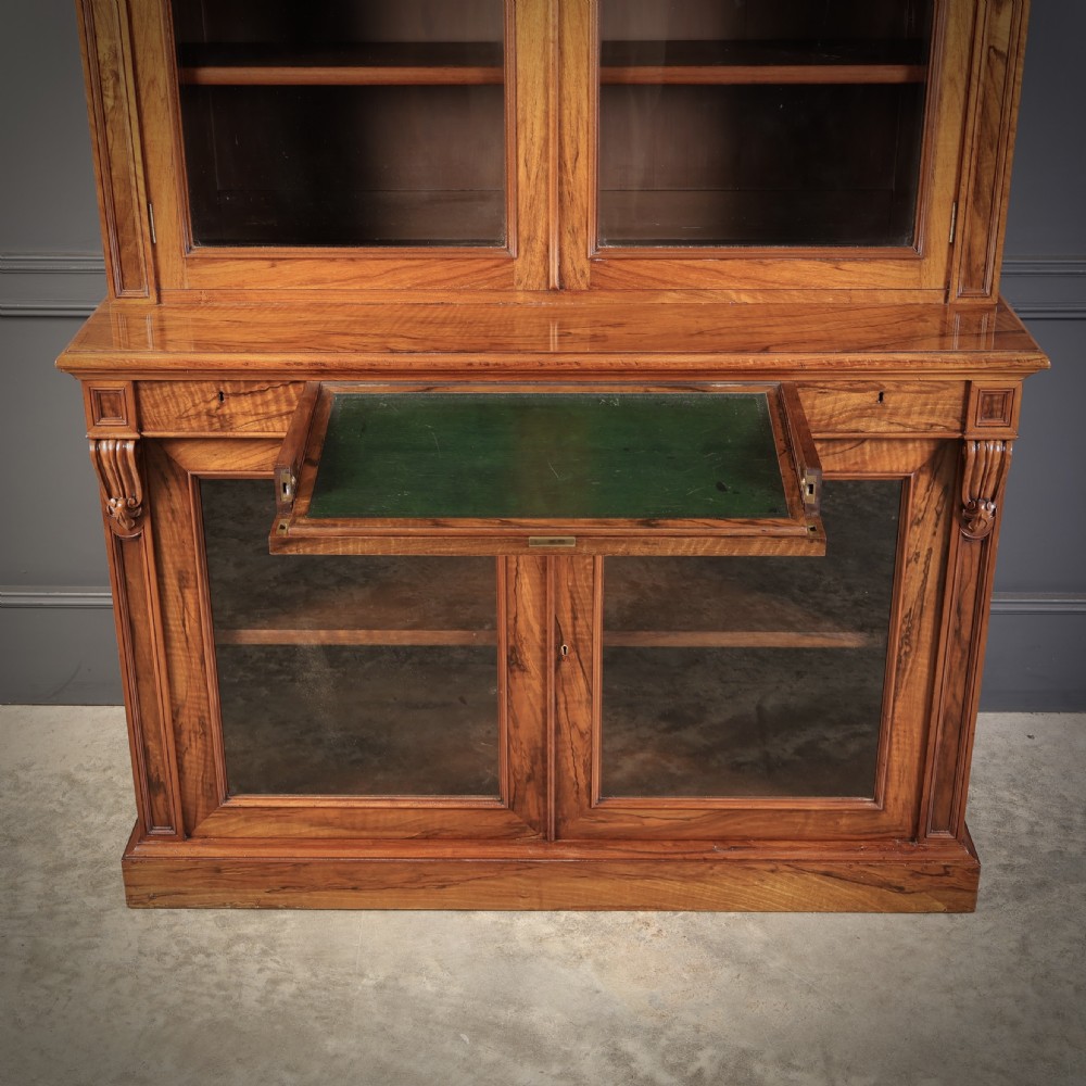 A two-part William IV walnut bookcase featuring upper and lower glazed doors with carved corbel accents and a plinth base. View V