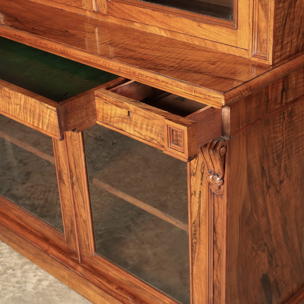 A two-part William IV walnut bookcase featuring upper and lower glazed doors with carved corbel accents and a plinth base. View XI