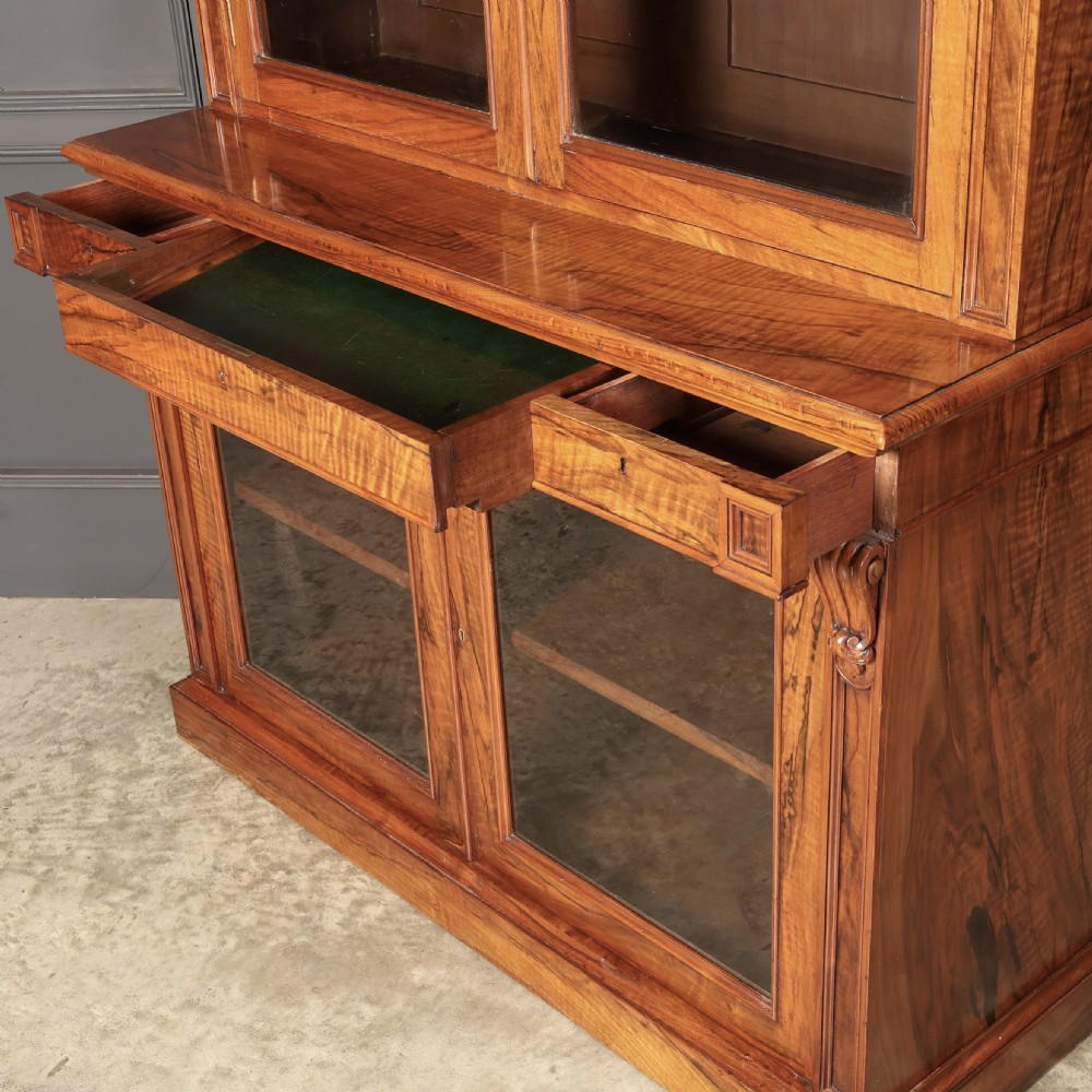 A two-part William IV walnut bookcase featuring upper and lower glazed doors with carved corbel accents and a plinth base. View XII