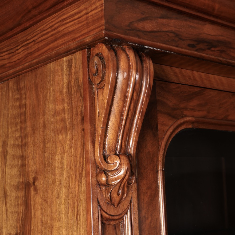A two-part William IV walnut bookcase featuring upper and lower glazed doors with carved corbel accents and a plinth base. View XVII