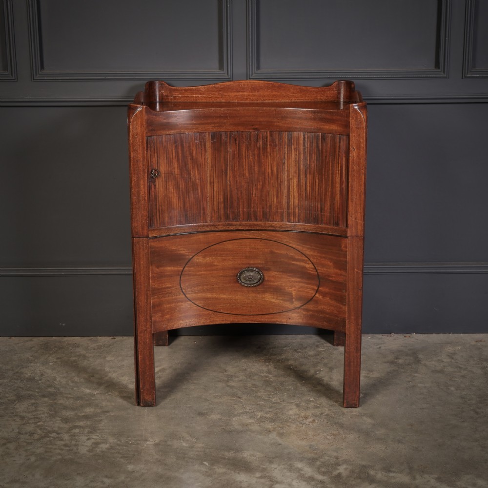 A George III mahogany nightstand featuring a gallery top, concave front with a tambour door, and a single lower drawer with oval inlay.