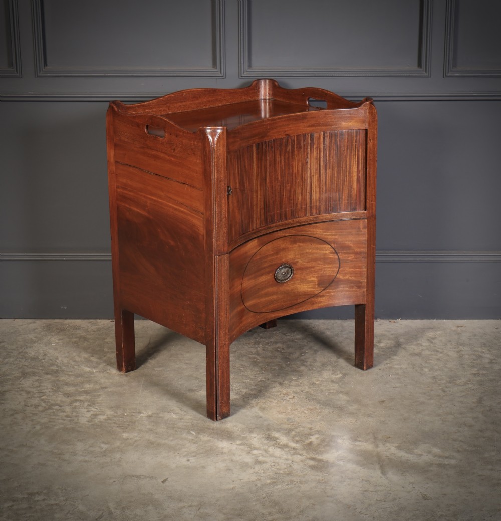 A George III mahogany nightstand featuring a gallery top, concave front with a tambour door, and a single lower drawer with oval inlay. View IV