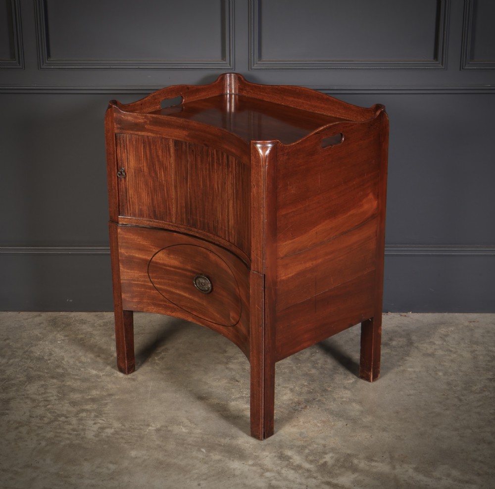 A George III mahogany nightstand featuring a gallery top, concave front with a tambour door, and a single lower drawer with oval inlay. View VI