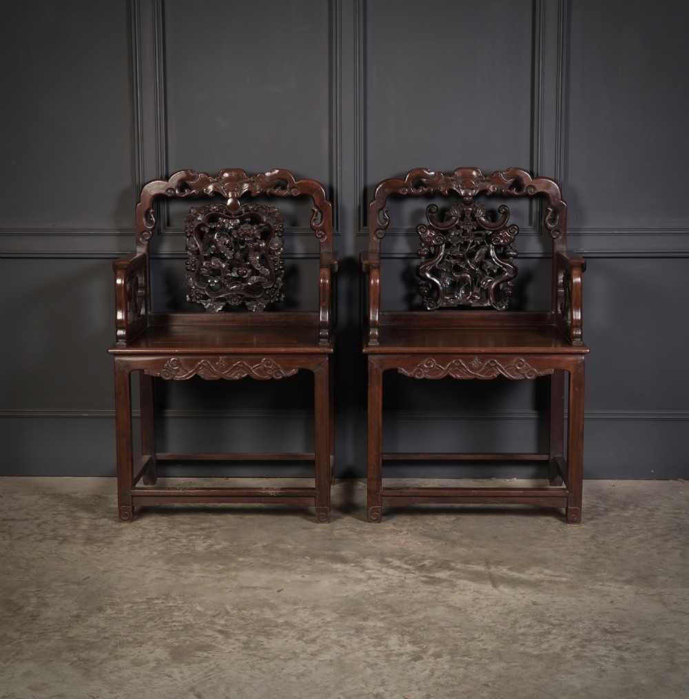 A pair of traditional Chinese dark hardwood Hongmu armchairs with intricately carved openwork back panels and rectangular seats.