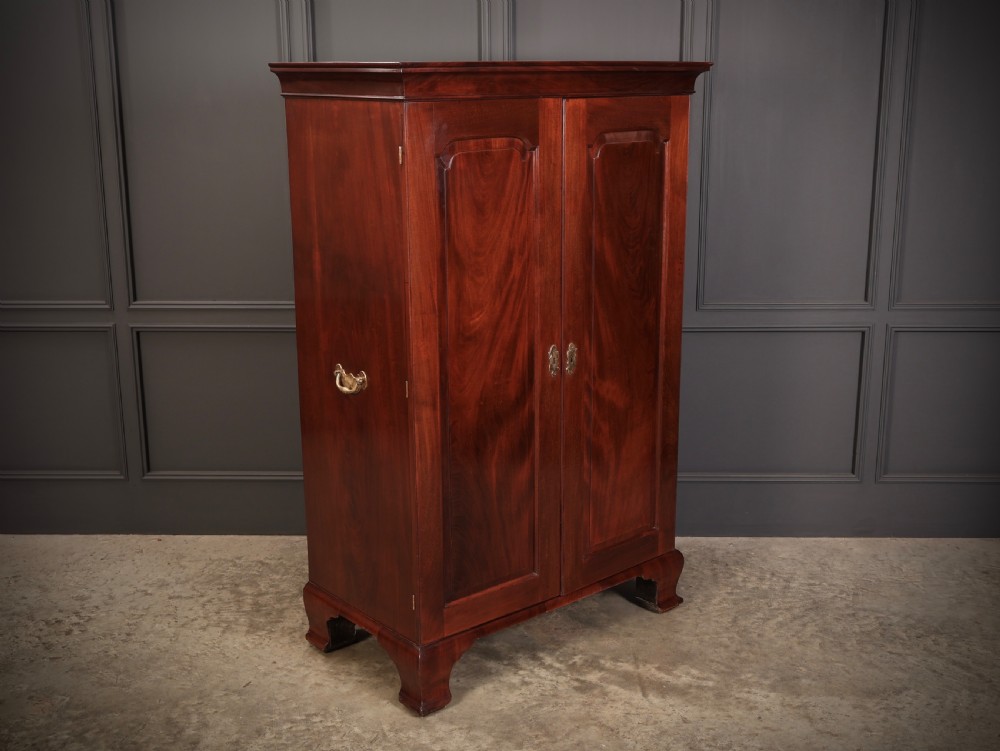 A George III mahogany estate cabinet shown with open panelled doors, revealing an interior with shelves on one side and multiple fitted drawers with brass ring handles on the other. View III