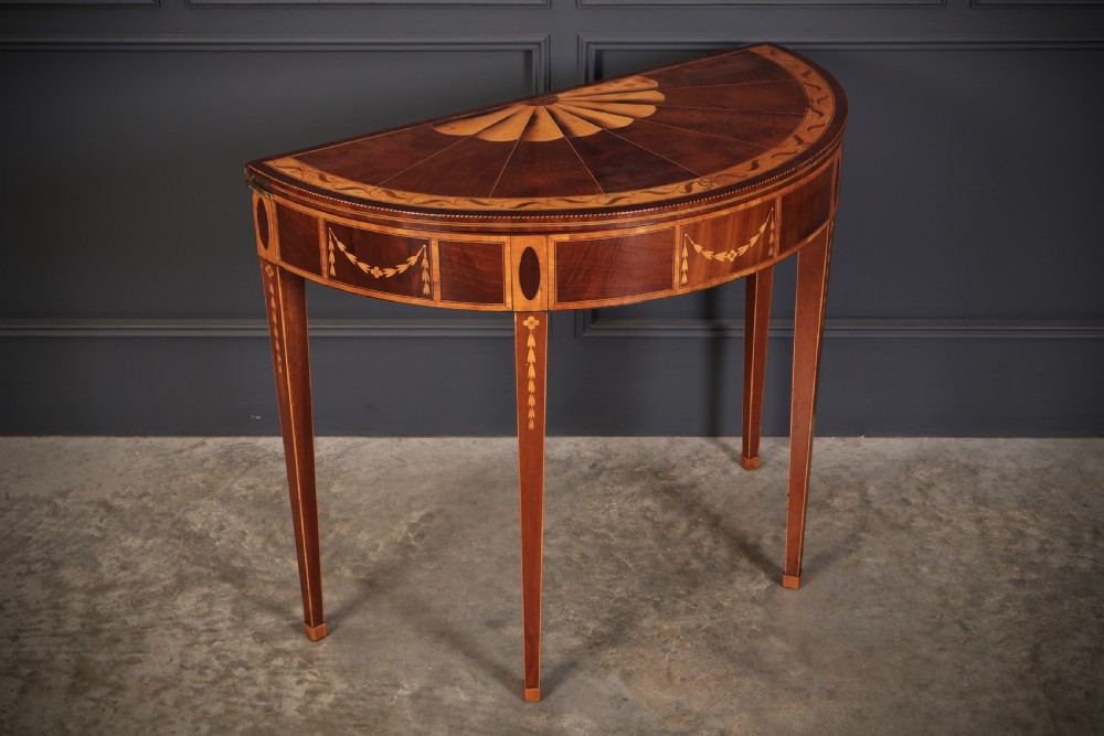 An 18th-century demilune tea table made of dark mahogany with satinwood marquetry inlays featuring a fan motif and tapered legs.