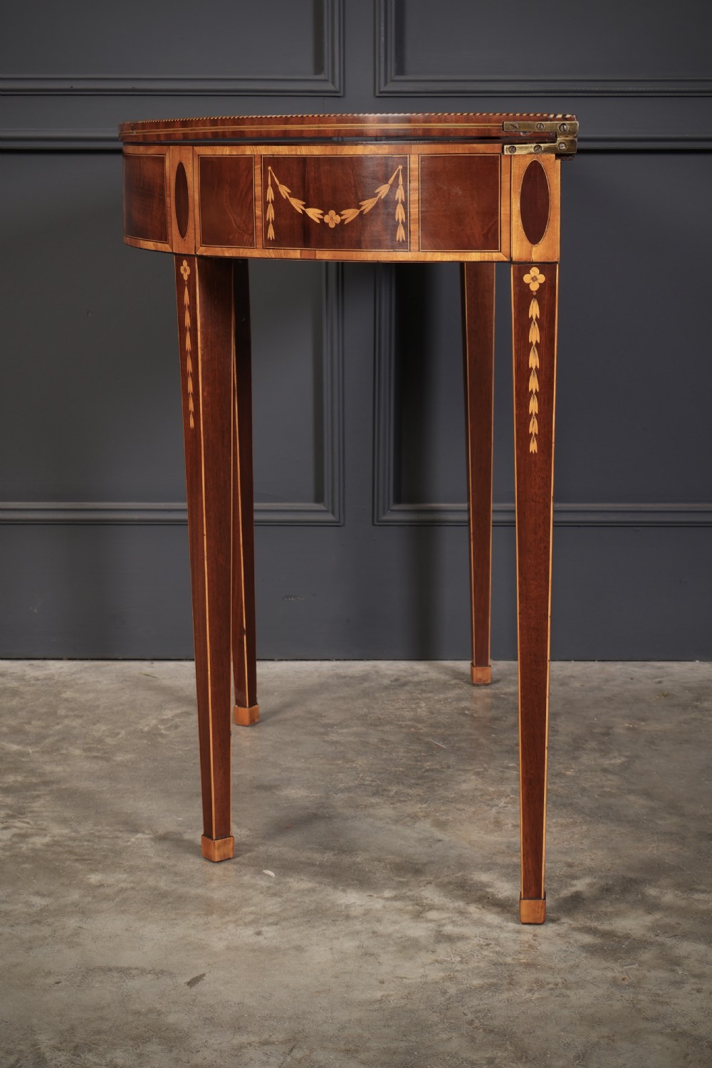 An 18th-century demilune tea table made of dark mahogany with satinwood marquetry inlays featuring a fan motif and tapered legs. View X