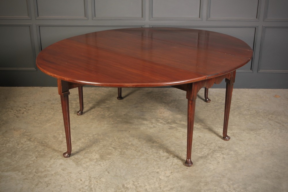 An 18th-century Georgian mahogany drop-leaf dining table with an oval top supported by tapered legs with pad feet.