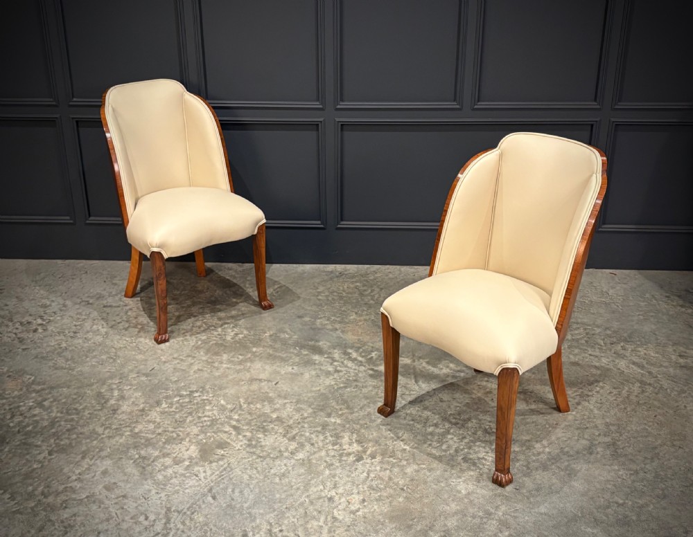 A pair of Art Deco armchairs featuring curved walnut veneer frames and cream leather upholstery.
