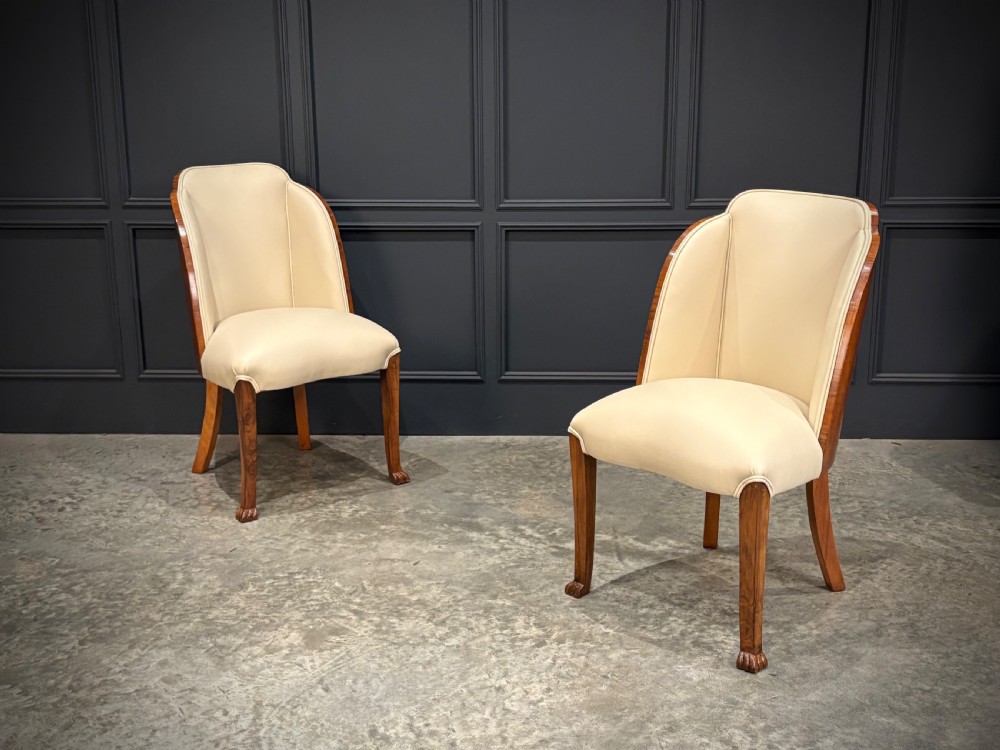 A pair of Art Deco armchairs featuring curved walnut veneer frames and cream leather upholstery. View II