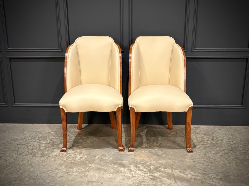 A pair of Art Deco armchairs featuring curved walnut veneer frames and cream leather upholstery. View V