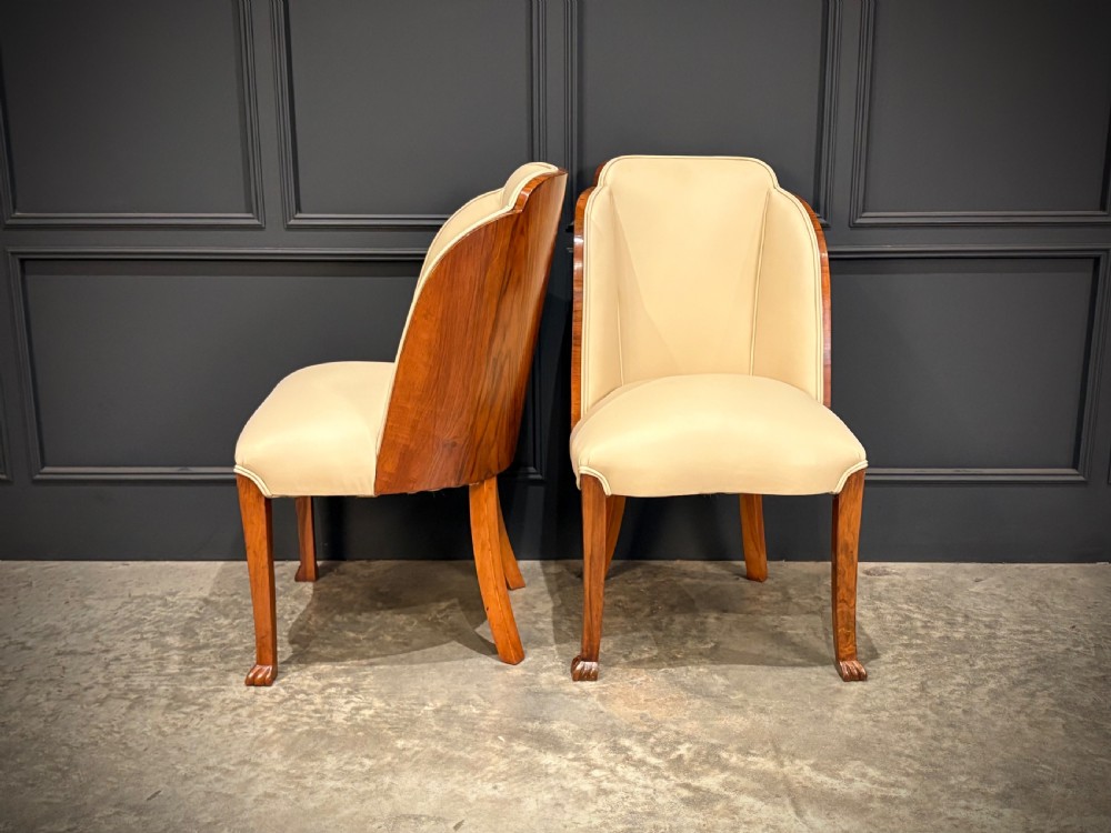 A pair of Art Deco armchairs featuring curved walnut veneer frames and cream leather upholstery. View VI