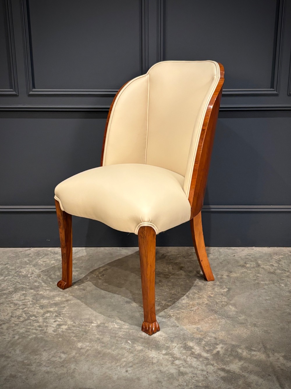 A pair of Art Deco armchairs featuring curved walnut veneer frames and cream leather upholstery. View IX