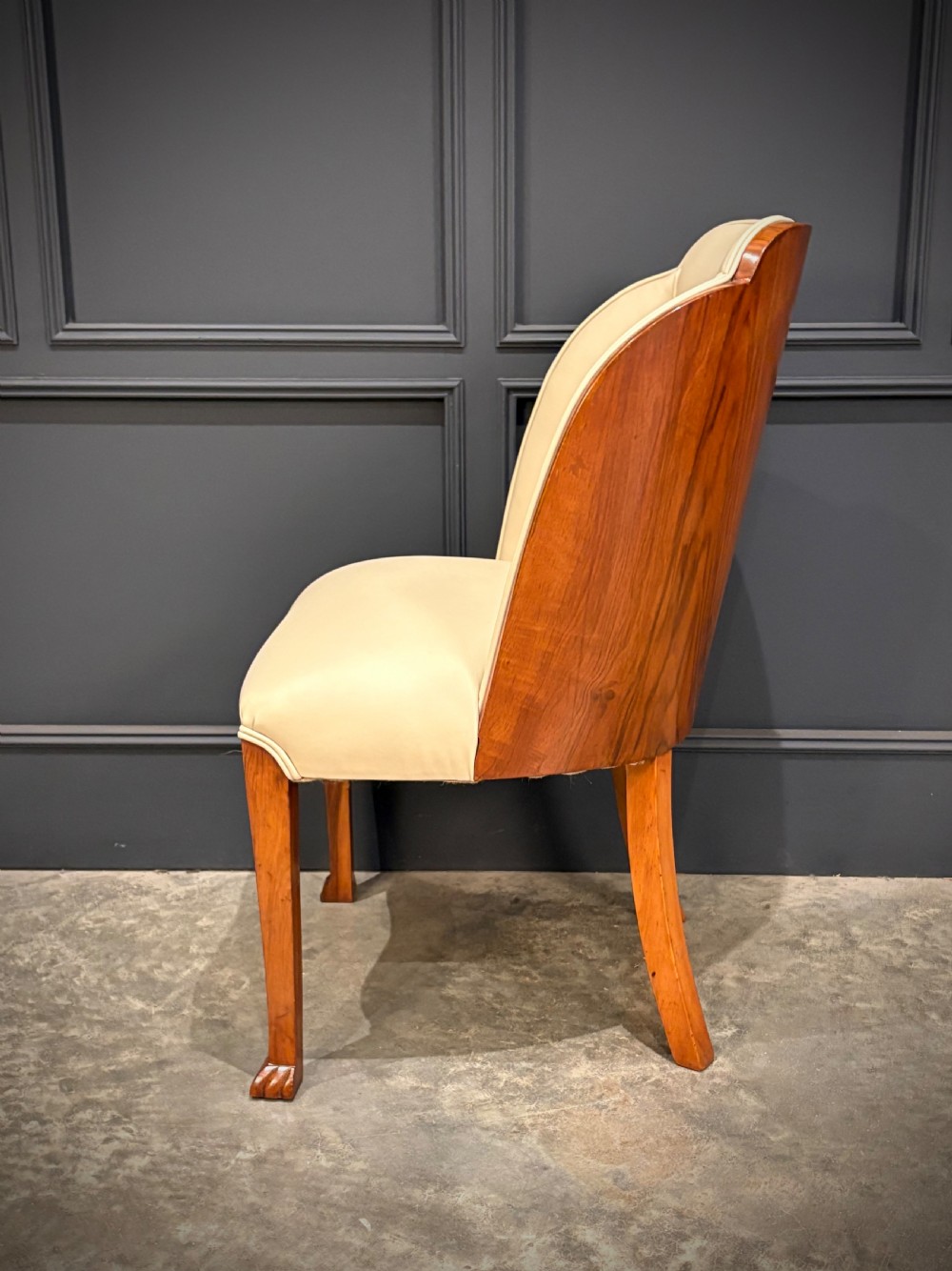 A pair of Art Deco armchairs featuring curved walnut veneer frames and cream leather upholstery. View X
