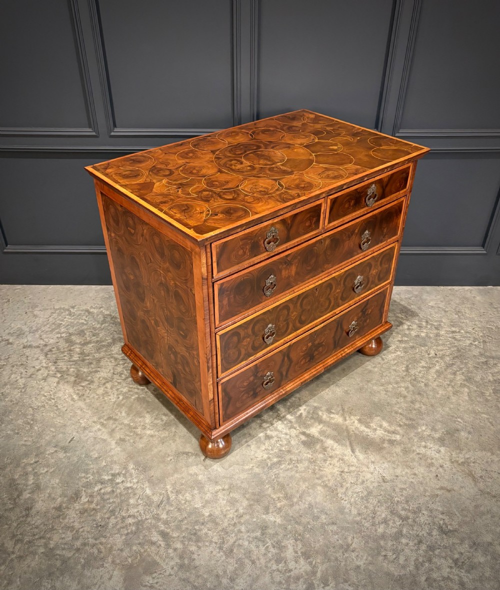 A late 17th-century William and Mary walnut chest of drawers featuring oyster veneered drawer fronts, geometric crossbanding, engraved brass drop handles, and turned bun feet. View II