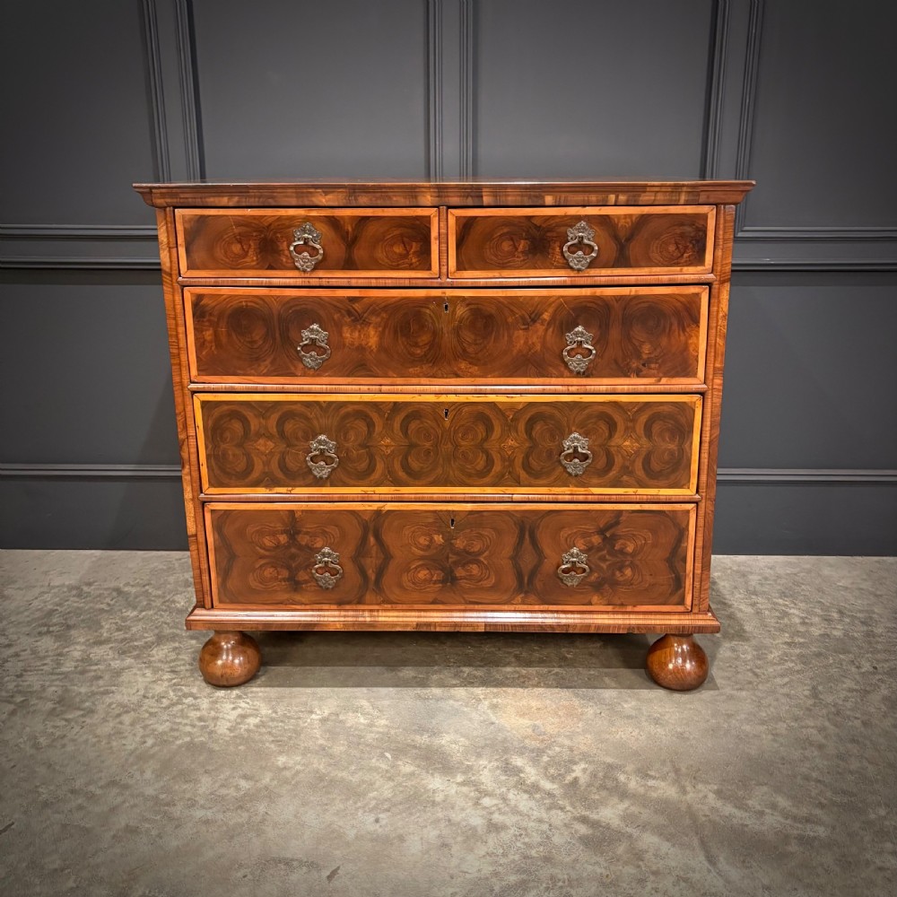 A late 17th-century William and Mary walnut chest of drawers featuring oyster veneered drawer fronts, geometric crossbanding, engraved brass drop handles, and turned bun feet. View V