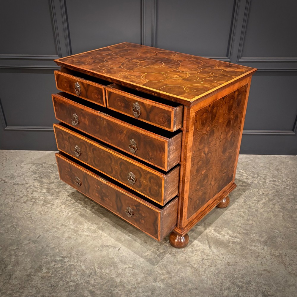A late 17th-century William and Mary walnut chest of drawers featuring oyster veneered drawer fronts, geometric crossbanding, engraved brass drop handles, and turned bun feet. View VIII