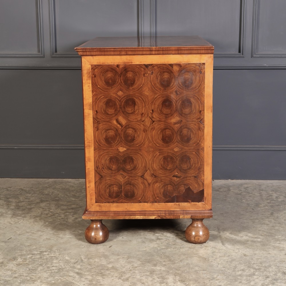 A late 17th-century William and Mary walnut chest of drawers featuring oyster veneered drawer fronts, geometric crossbanding, engraved brass drop handles, and turned bun feet. View X