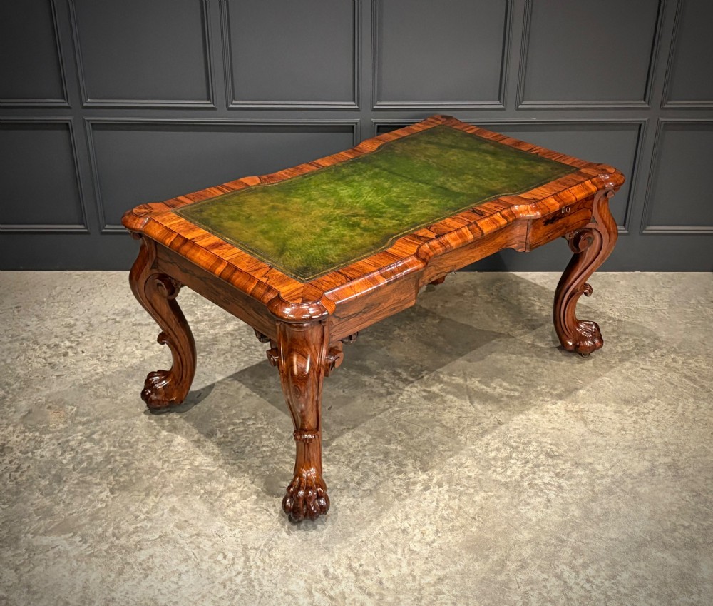 A William IV rosewood partners writing desk featuring a green leather inset top, carved serpentine aprons, and bold cabriole legs ending in carved feet.