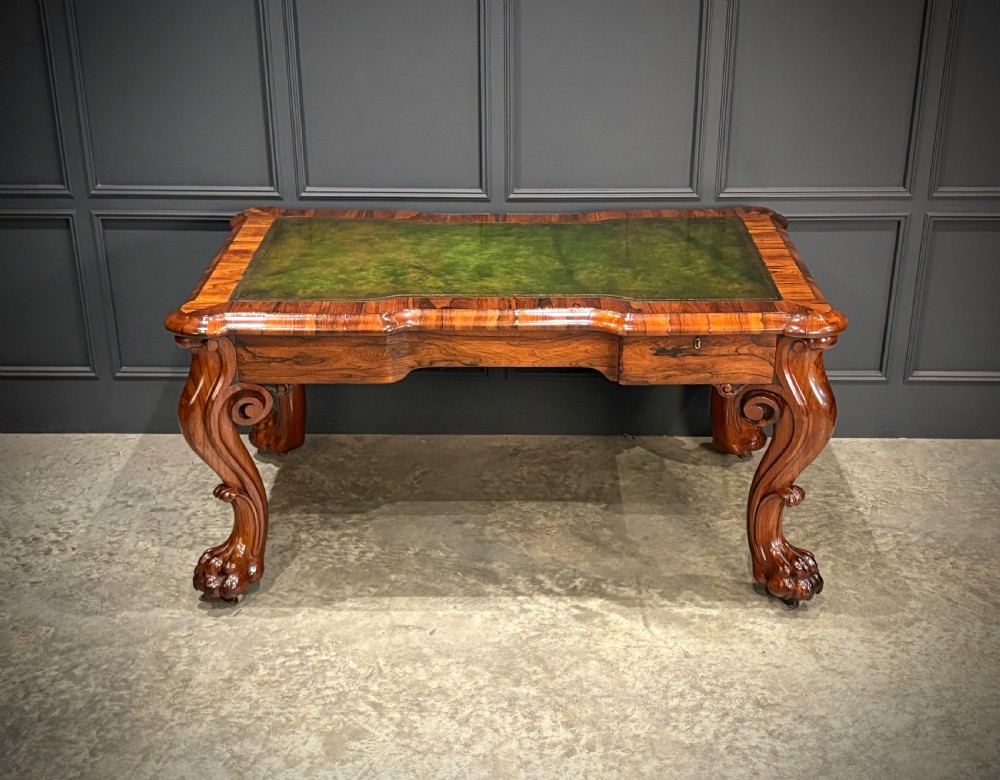 A William IV rosewood partners writing desk featuring a green leather inset top, carved serpentine aprons, and bold cabriole legs ending in carved feet. View VII