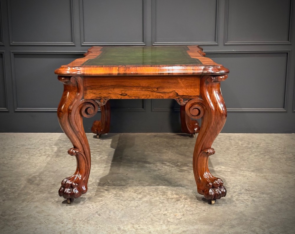 A William IV rosewood partners writing desk featuring a green leather inset top, carved serpentine aprons, and bold cabriole legs ending in carved feet. View XI