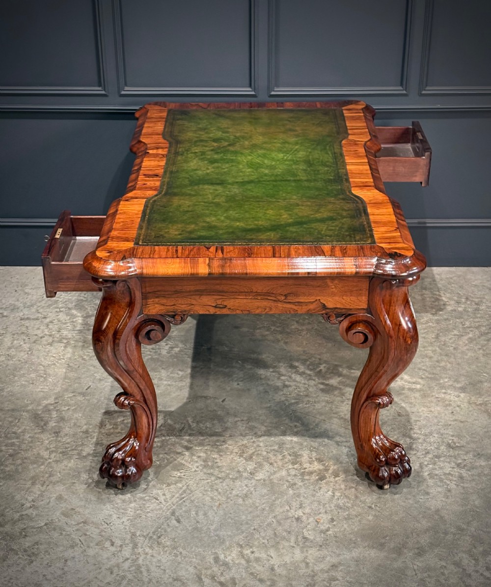 A William IV rosewood partners writing desk featuring a green leather inset top, carved serpentine aprons, and bold cabriole legs ending in carved feet. View XIV