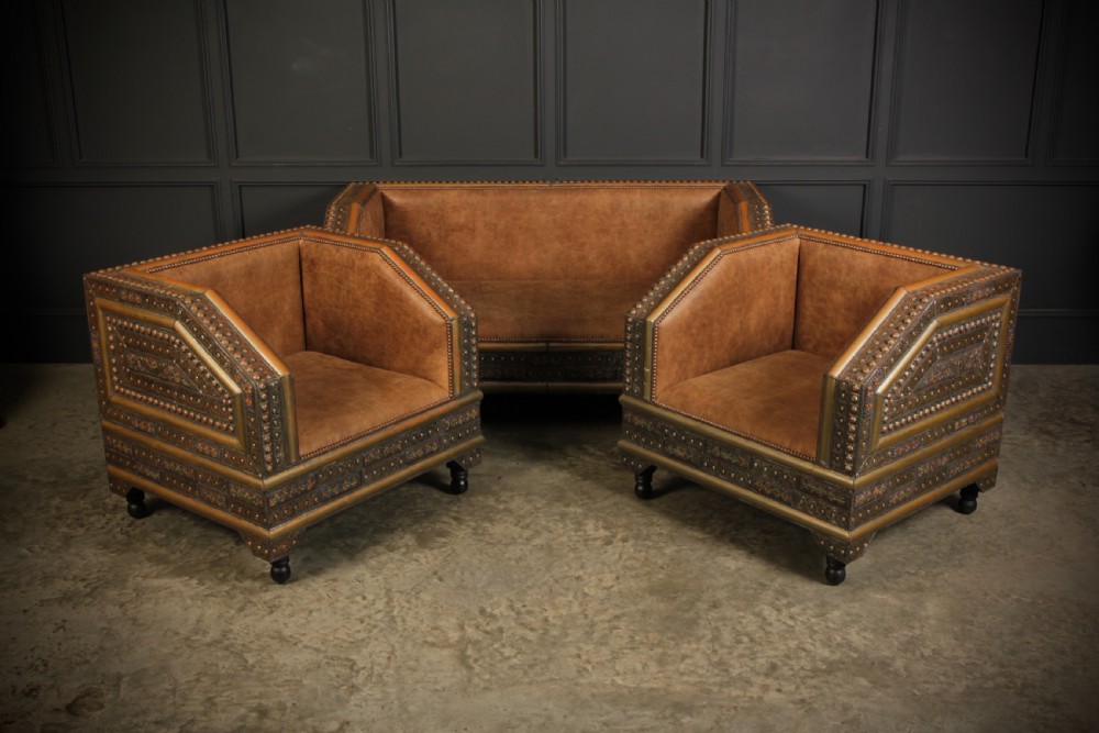 A three-piece Moroccan seating suite comprising a sofa and two armchairs upholstered in tan leather with brass studding and geometric metal trim.