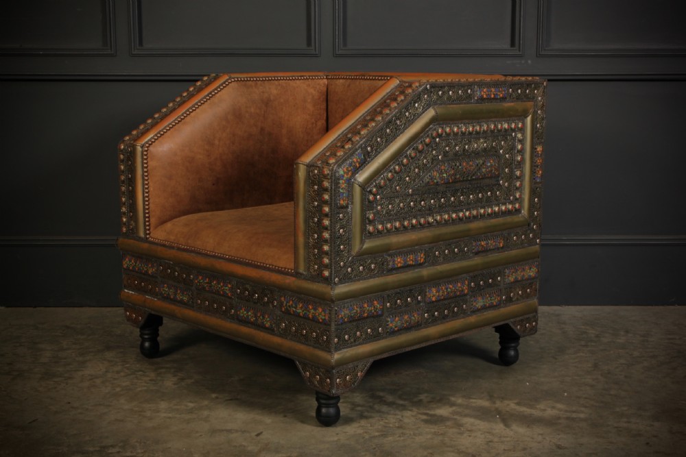 A three-piece Moroccan seating suite comprising a sofa and two armchairs upholstered in tan leather with brass studding and geometric metal trim. View IX