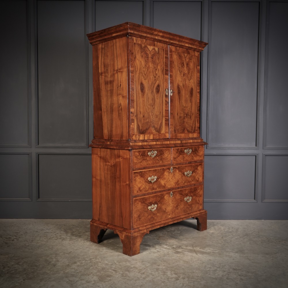 A two-part Queen Anne walnut cabinet on chest featuring upper cupboard doors with bookmatched timber grain and a lower chest with four drawers on bracket feet. View VI