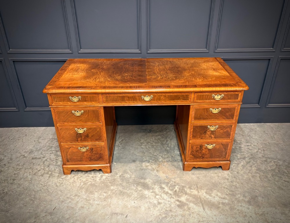An antique burr walnut pedestal desk featuring inlaid feather-banded borders, brass drop handles, and multiple side drawers. View V