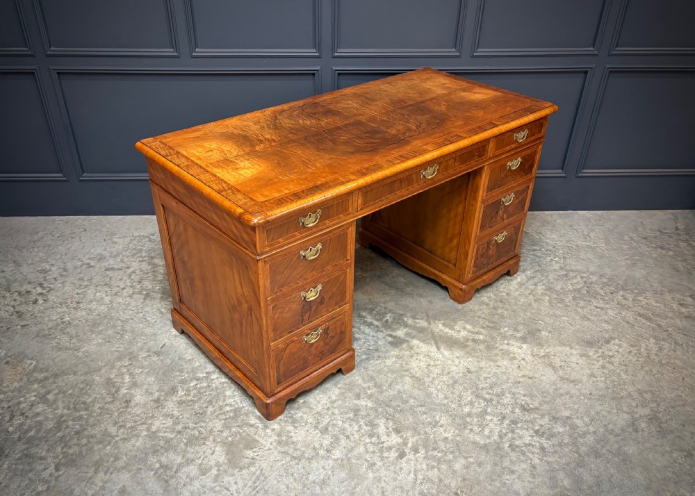 An antique burr walnut pedestal desk featuring inlaid feather-banded borders, brass drop handles, and multiple side drawers.