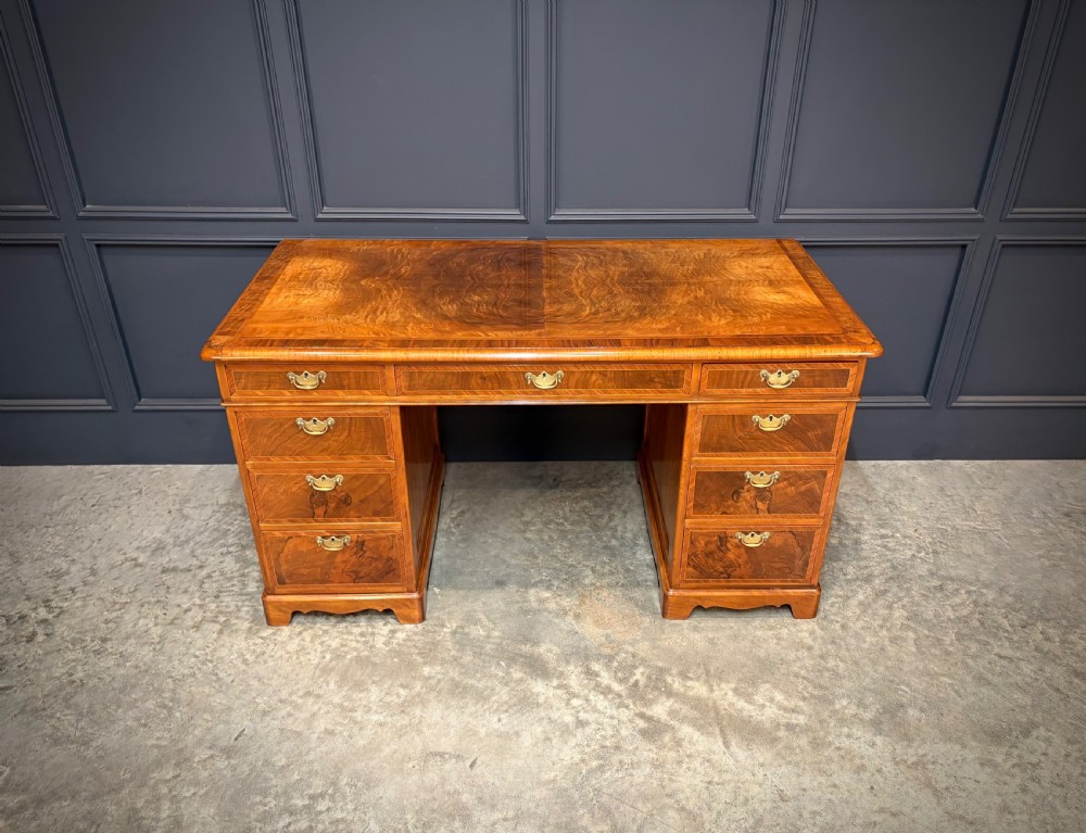 An antique burr walnut pedestal desk featuring inlaid feather-banded borders, brass drop handles, and multiple side drawers. View III