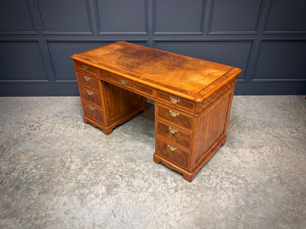 An antique burr walnut pedestal desk featuring inlaid feather-banded borders, brass drop handles, and multiple side drawers. View VIII