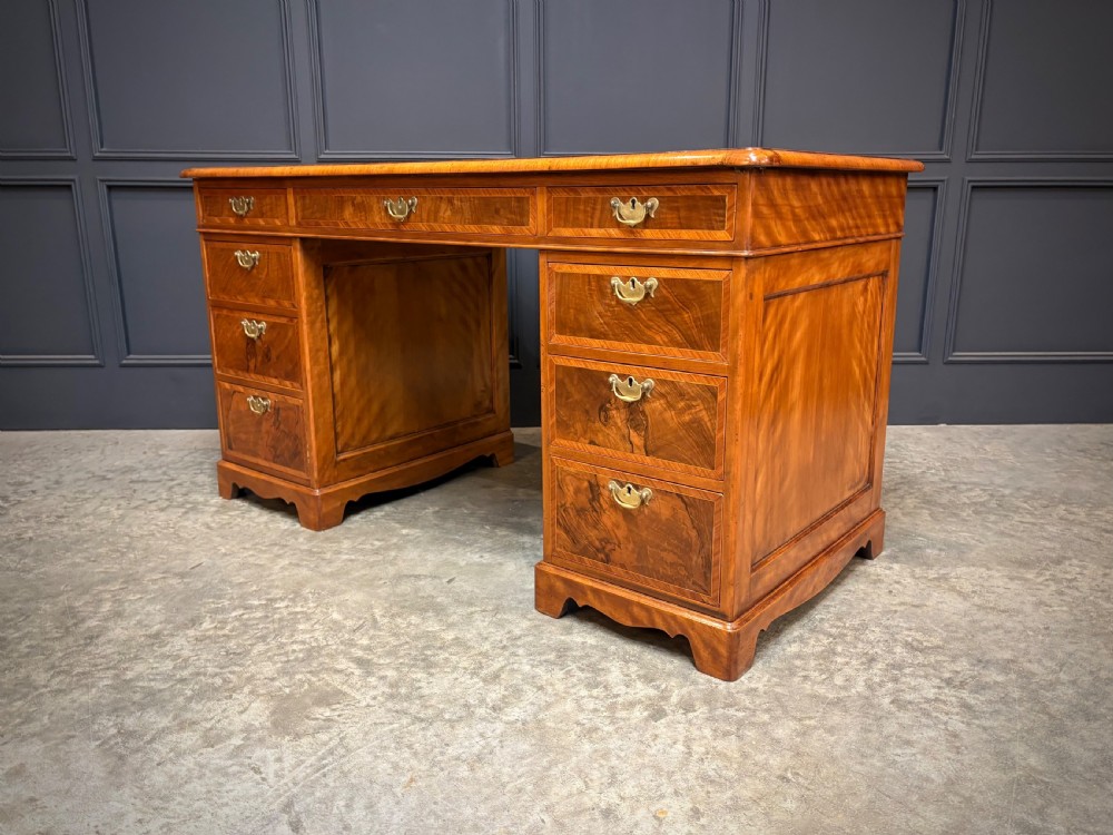 An antique burr walnut pedestal desk featuring inlaid feather-banded borders, brass drop handles, and multiple side drawers. View IX