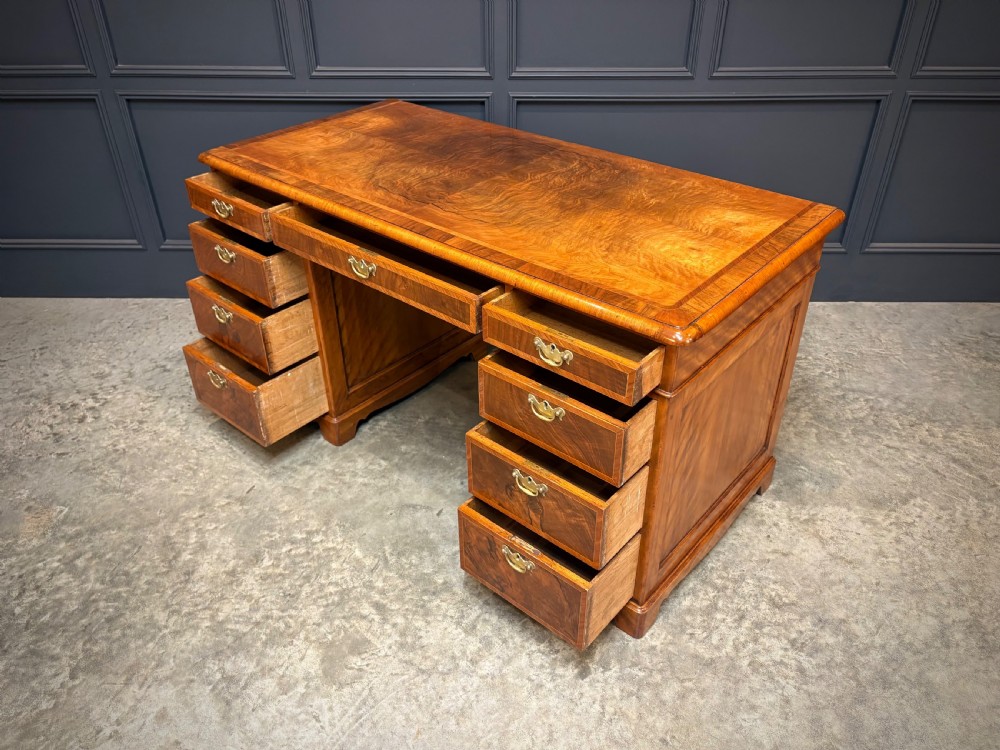 An antique burr walnut pedestal desk featuring inlaid feather-banded borders, brass drop handles, and multiple side drawers. View XI